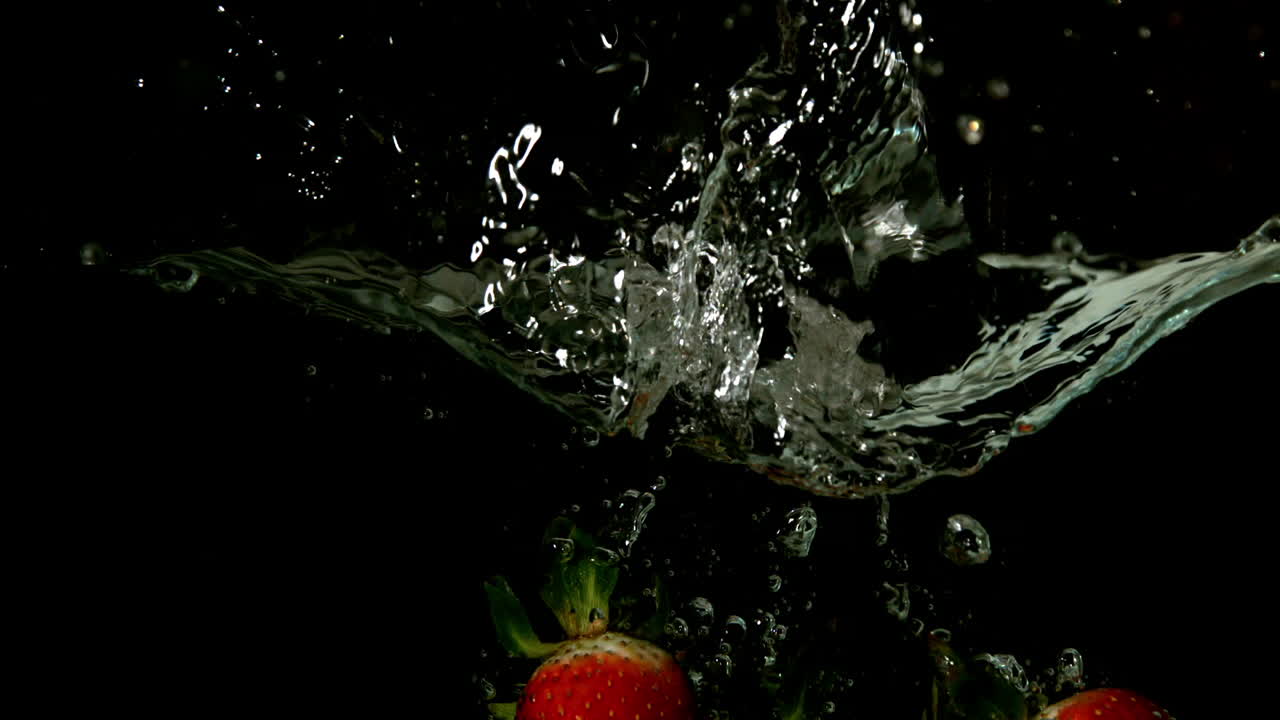 fresas cayendo en el agua sobre un fondo negro