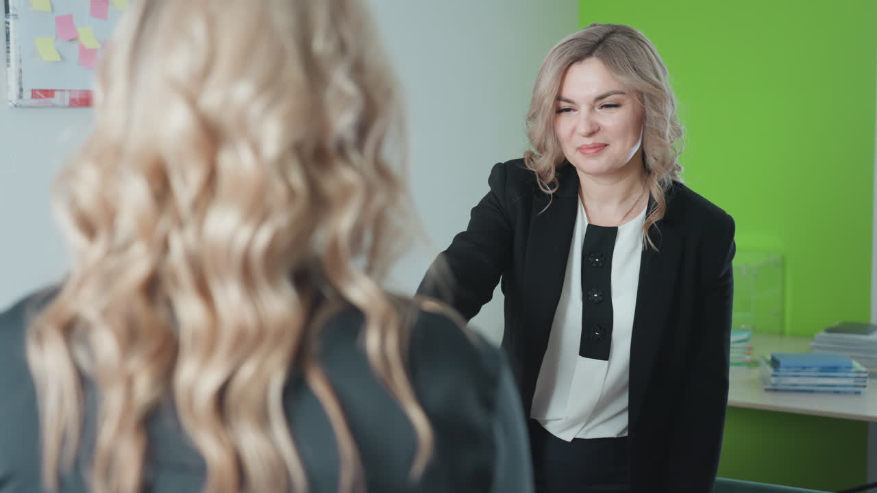 lady rises to present key near building miniature as client stretches hand to receive key, both sharing warm handshake beside pen holder on office table, highlighting property handover moment