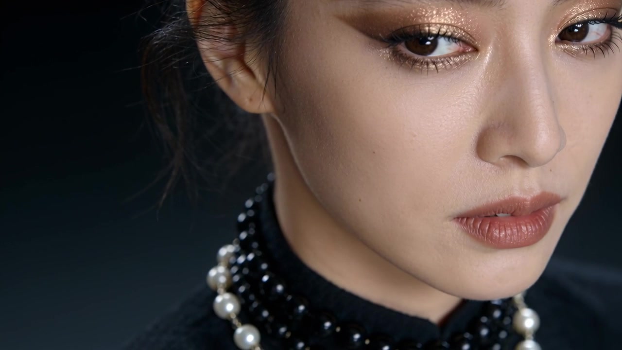 Modella con top a collo alto che reagisce alla telecamera, inclinando la testa e abbassando lo sguardo in studio, con perle.