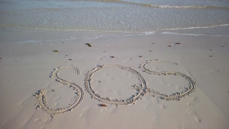 turning shot of sos written in the sand on a beach