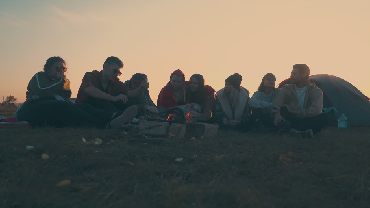 excursionistas alegres pasan el tiempo en el campamento con una hoguera ardiendo