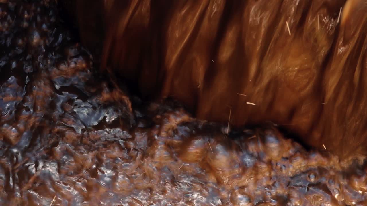 wastewater flowing over the edge of a treatment basin, showing dark liquid with a foamy, brown surface