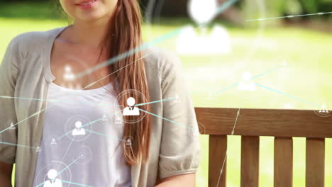 animation of network of connected icons in circles over happy caucasian woman sitting on bench