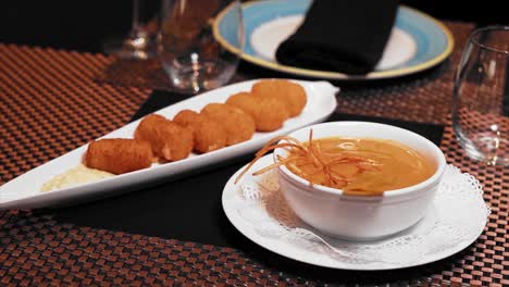 cream soup of the day accompanied with ham croquettes on the table along with crystal glasses in a luxury restaurant