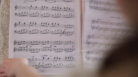 young musician flips through sheet music playing piano