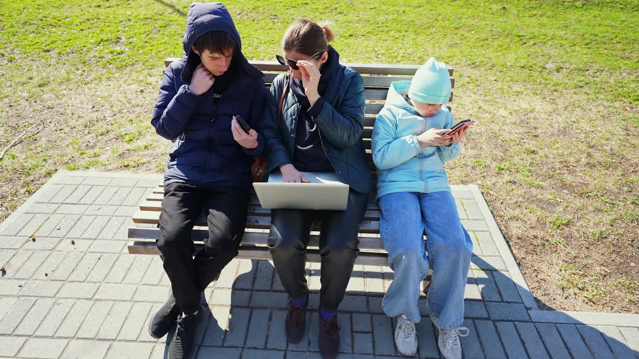 Tre personer fordypet i digitale enheter på en parkbenk