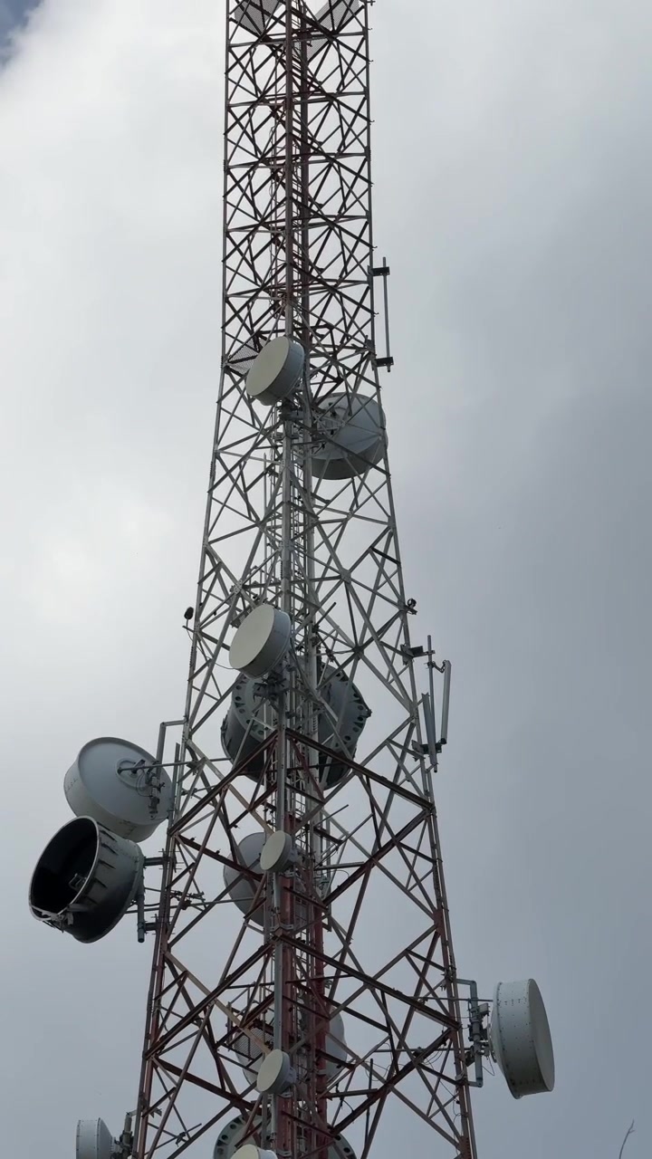 Alta torre di telecomunicazioni con antenne paraboliche su sfondo di cielo nuvoloso