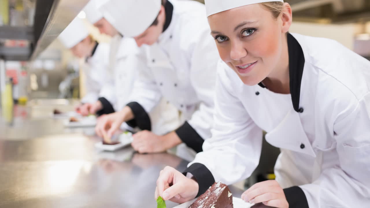 una chef caucásica sonriente con un delantal preparando comida en una cocina profesional