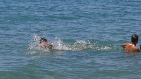 medium , follow pan , slow motion 100fps footage of two caucasian brothers swimming at crystal clear blue waters, enjoying they summer vacations