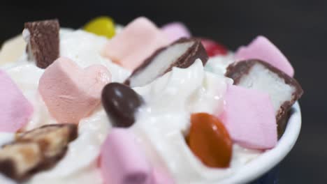 close-up sweet dessert with cream and marshmallows on a rotating table on black background.