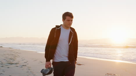 young man walking along beach as sun rises over ocean