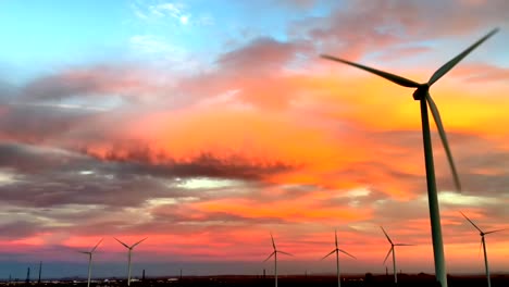 green energy wind turbine blades rotate against dramatic orange sunset sky