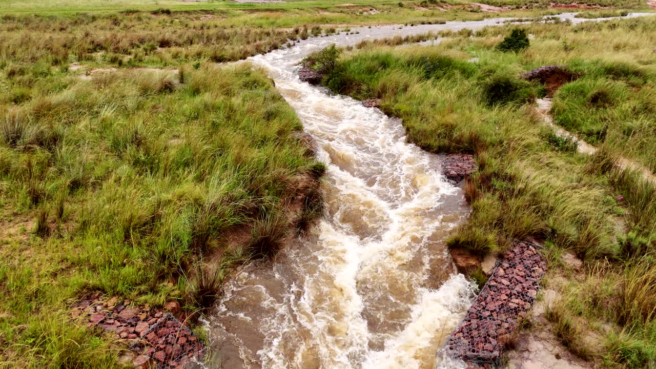 Gabions used to prevent soil erosion, floodwaters rage over rural grassy terrain