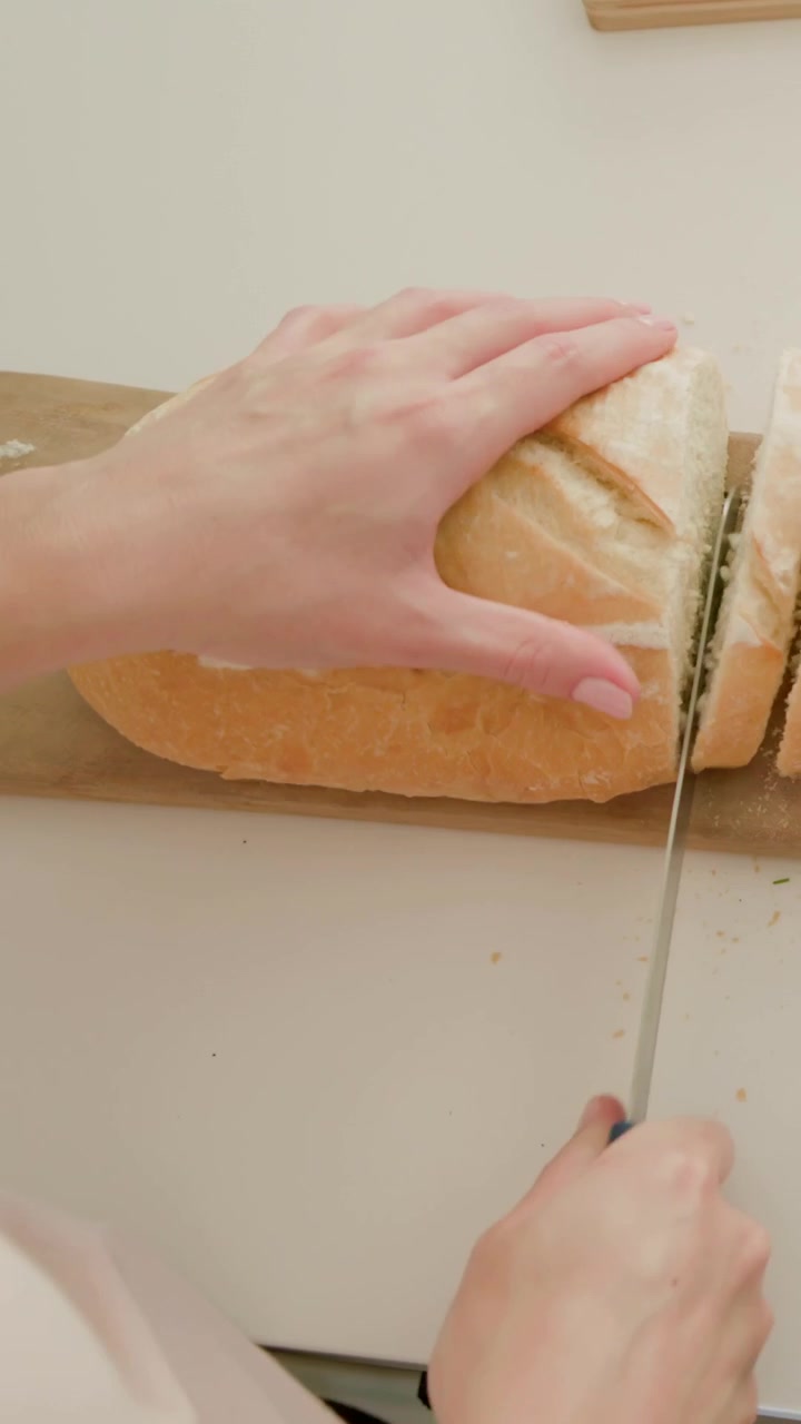Vertical video: Positioning knife, hands holding loaf and sawing on cutting board to slice in top