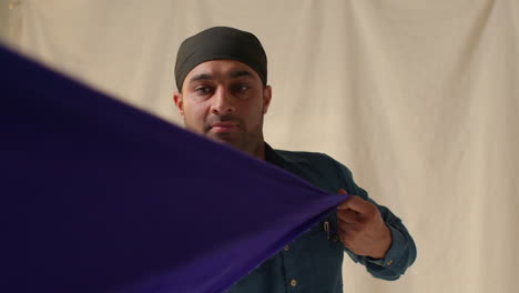 studio shot of sikh man folding fabric for turban against plain background 3