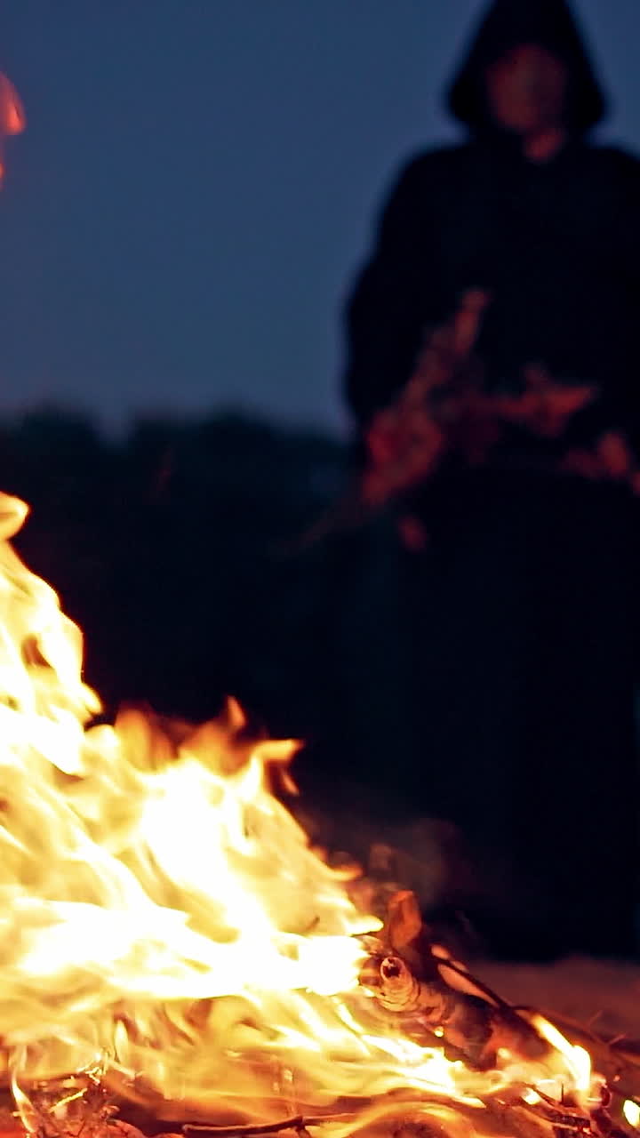 Witch in black near bonfire. Mystical witch walking around bonfire. Vertical video