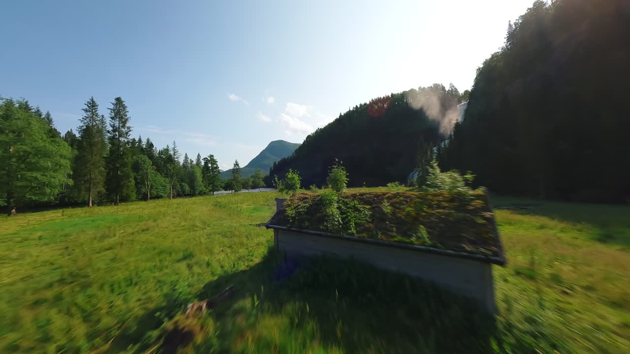 Drone FPV che vola verso una cascata attraverso un campo verde