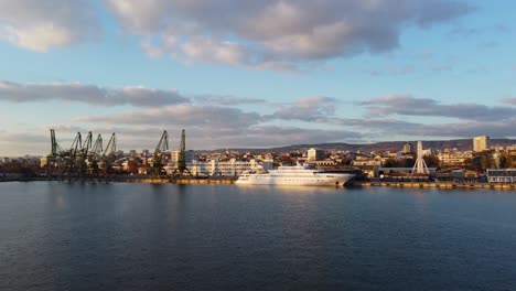 White-Yacht-in-Port-of-Varna-drone-shot-flying-towards-boat-and-pier-with-cloudy-sky