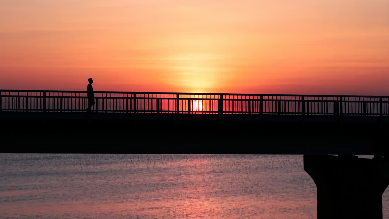 Silhouette of a Person Walking on a Bridge at Sunset