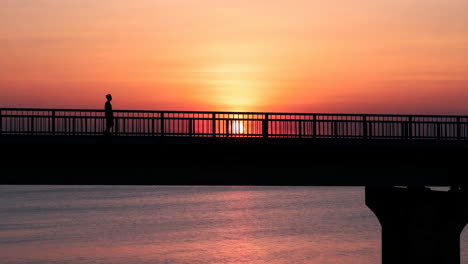 silhouette of a person walking on a bridge at sunset
