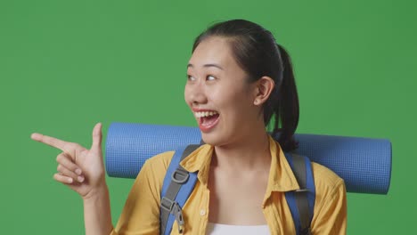 woman pointing and smiling with a backpack and yoga mat