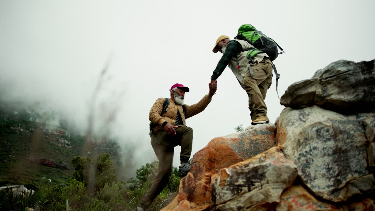 Two men hiking on a mountain, helping each other climb