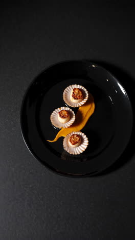 seared scallops with orange puree on a black plate