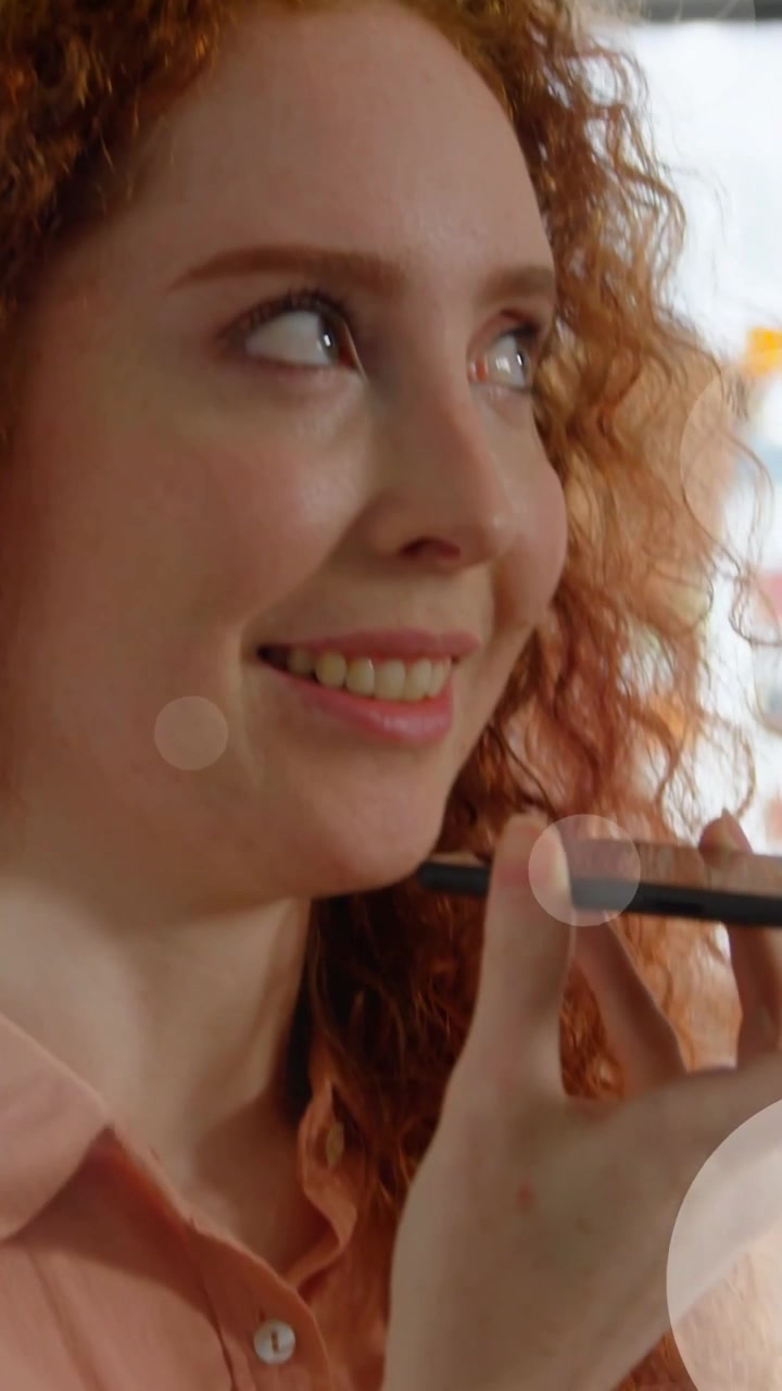 Vertical video: Woman holding phone, speaking then smiling, causing bokeh revealing tiles for tech