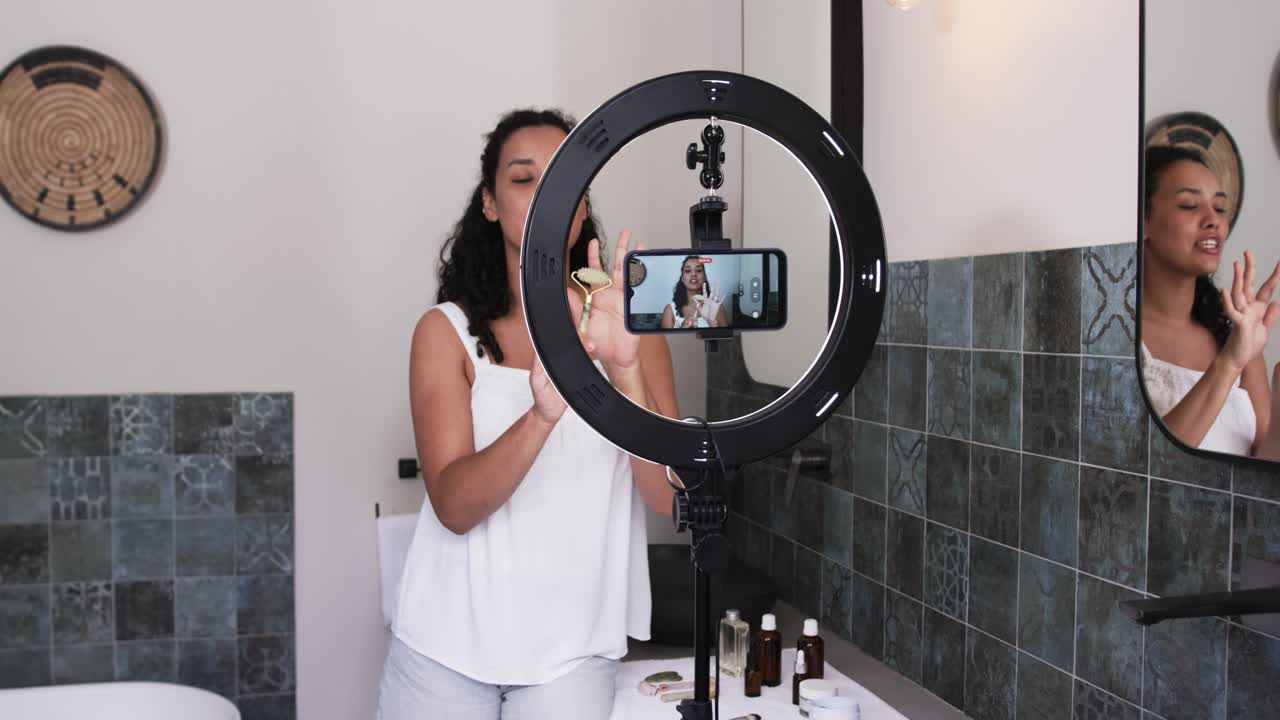 Donna afroamericana adulta che sistema il telefono su un ring light, che filma e applica prodotti per la cura della pelle.