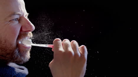 slow motion backlit - a man brushing teeth sending many particles into the air