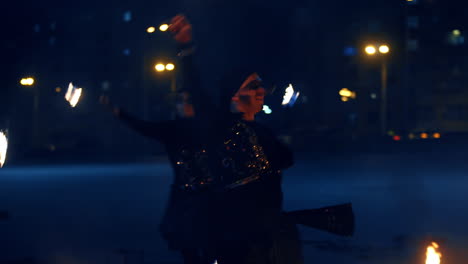 people wearing black costumes dance with burning balls on the chains. fire show presented outdoors at night.