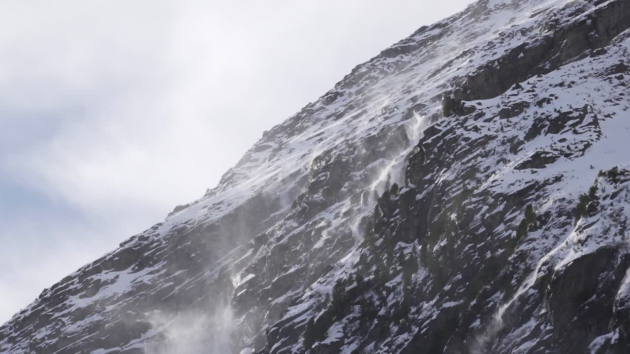Close up of snow getting blown off a mountain cliff ridge on a snowy rocky glacier slope