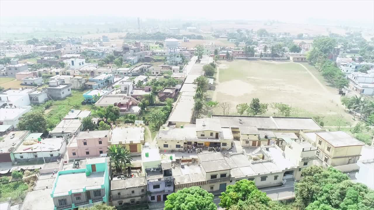 Aerial view of a village with houses, trees, a road, and a field
