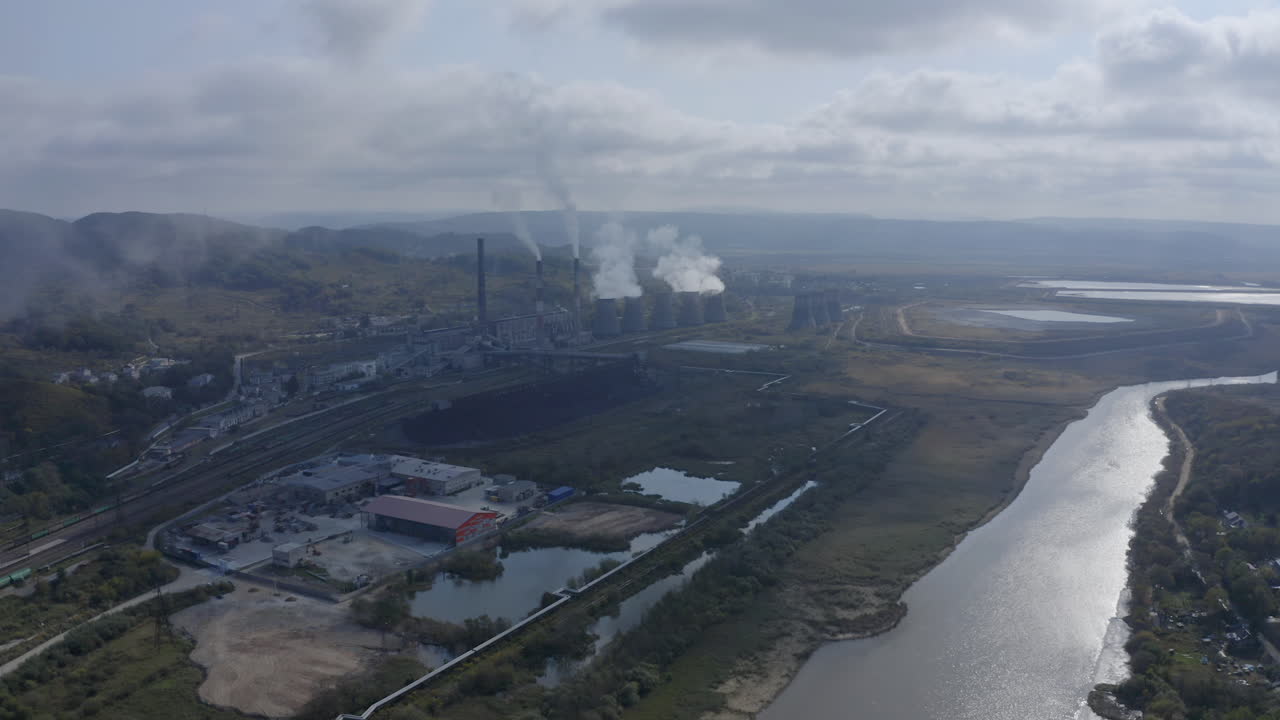 Vista paisajística con una central termoeléctrica de carbón con sus chimeneas emitiendo humo blanco al aire en un día soleado y nublado.