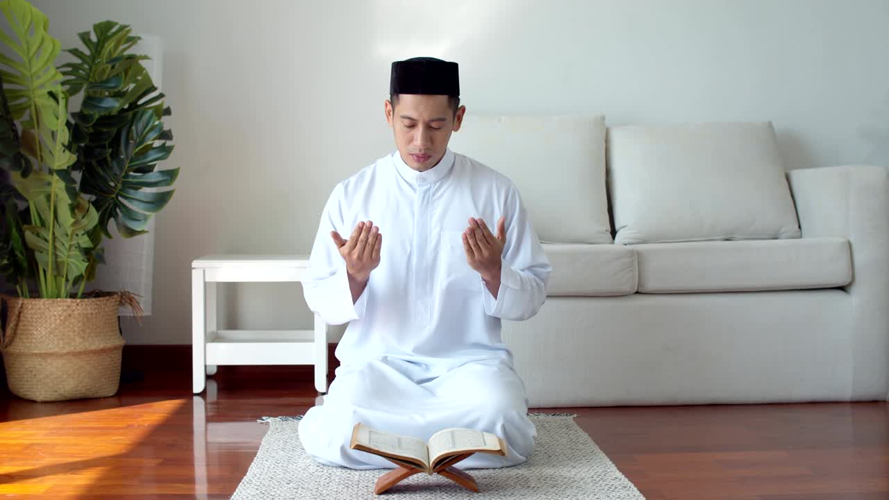 이슬람 옷을 입은 젊은 이슬람 남자가 꾸란을 읽고 기도하고 있습니다.