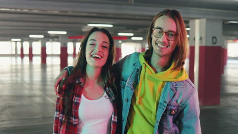 happy young stylish man and woman looking at each other with love, then hug and smile at the camera in a empty parking