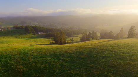 Sun-rays-and-evening-haze-over-green-hills-in-rural-California,-golden-hour-aerial-view