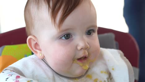 un niño pequeño en su asiento comiendo su comida para bebés en cámara lenta, primer plano