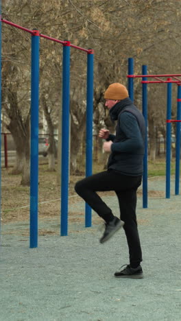 un entrenador realiza un ejercicio de ritmo rápido solo en un estadio al aire libre, con una gorra marrón y un traje negro, está rodeado de barras de hierro azules y rojas alrededor