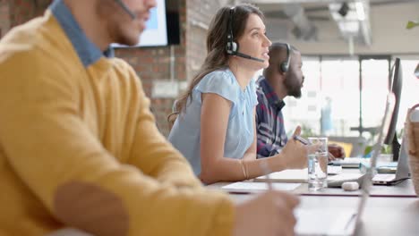 Caucasian-businesswoman-talking-on-phone-headset-sitting-on-her-desk-at-office