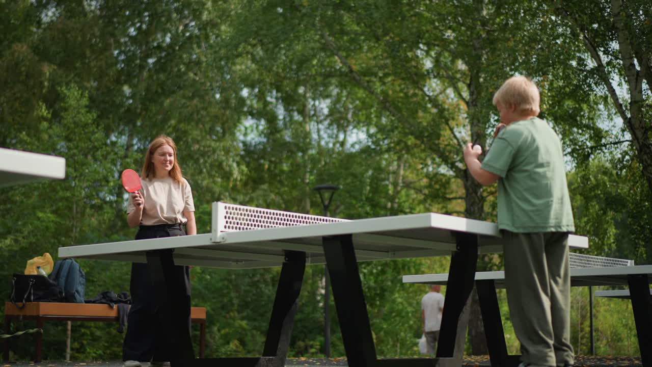 Lively Children Enjoying Table Tennis, Young Girl With Bright Hair And Smiling Boy Engaging In Outdoor Table Tennis, Enthusiastic Girl With Fiery Hair And Joyful Boy Sharing Game In Park