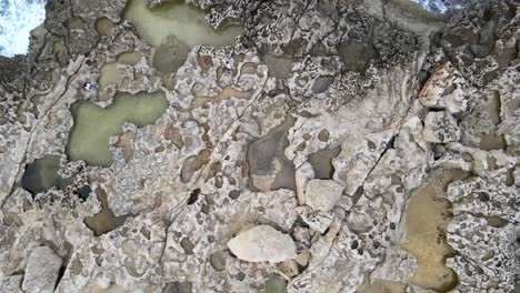 Aerial-top-view-of-two-tourists-on-natural-shaped-rocks-in-Dwejra-Bay,-maltese-island-of-Gozo