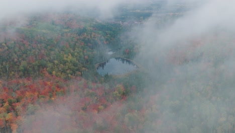 Drohne-Fliegt-Durch-Neblige-Wolken-Und-Enthüllt-Den-Herbstwald-Und-Den-Teich-In-Der-Mitte