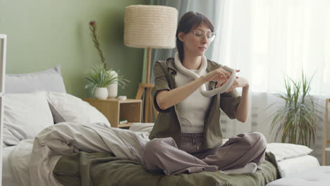 young woman holding her white pet snake while sitting on bed at home