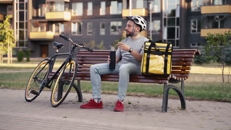 Repartidor-De-Alimentos-Hombre-Sentado-En-Un-Banco-Tomando-Una-Taza-De-Té-Durante-Su-Descanso