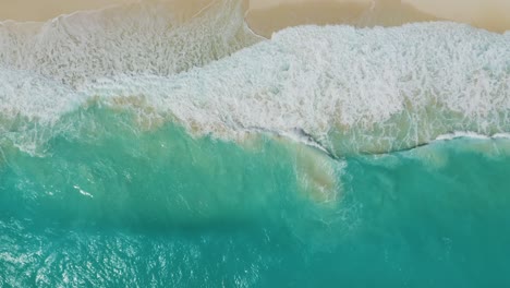 drone descends as waves crash on tropical white sand beach