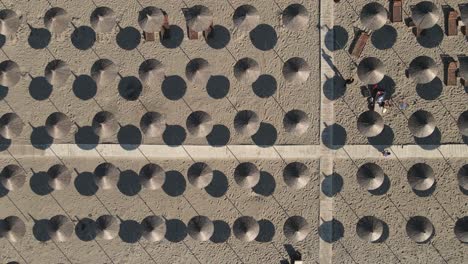 Rising-sand-aerial-reveals-geometric-pattern-of-grass-beach-umbrellas