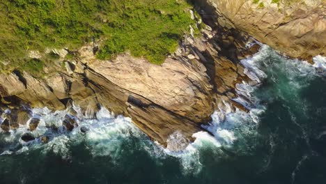 aerial top down view of sea waves hitting on the low cliffs near bombinhas