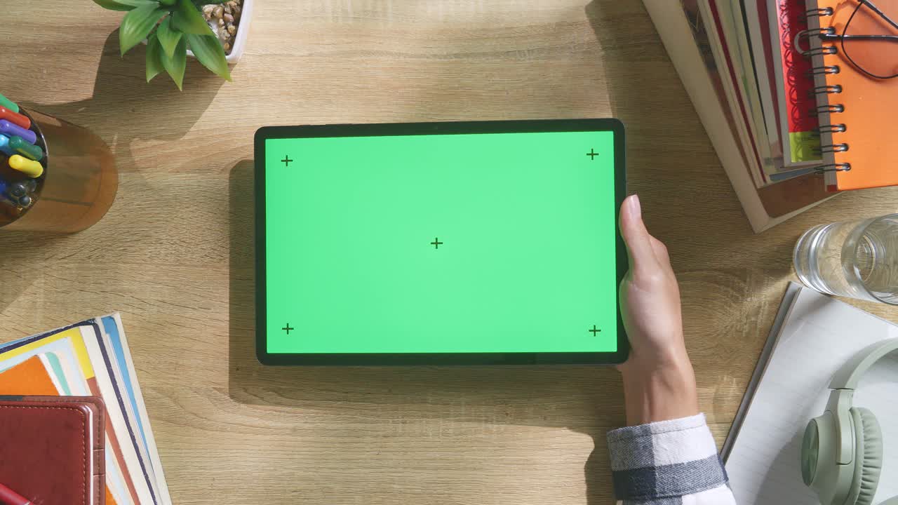 vista de arriba hacia abajo de una computadora portátil con pantalla verde simulada pantalla chromakey en un escritorio de oficina de madera al lado de la libreta con bolígrafos, gafas y un vaso de agua.