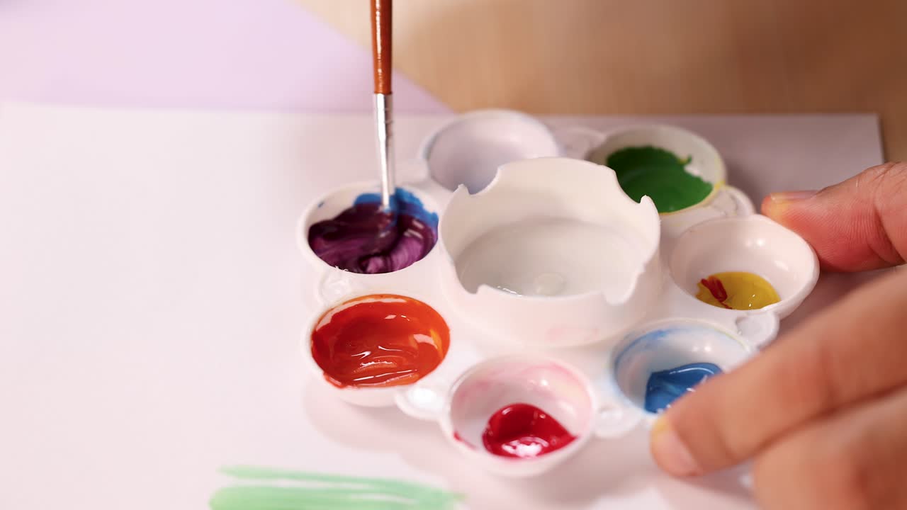 Artist hand mixes vibrant watercolor paints on palette under soft lighting, close-up, steady camera